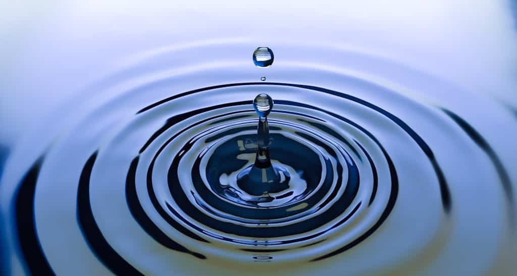A stunning close-up of a water droplet creating ripples on a smooth water surface, capturing nature's simplicity.
